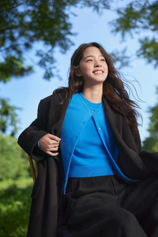 Woman wearing blue merino wool cardigan outdoors with black coat in a park