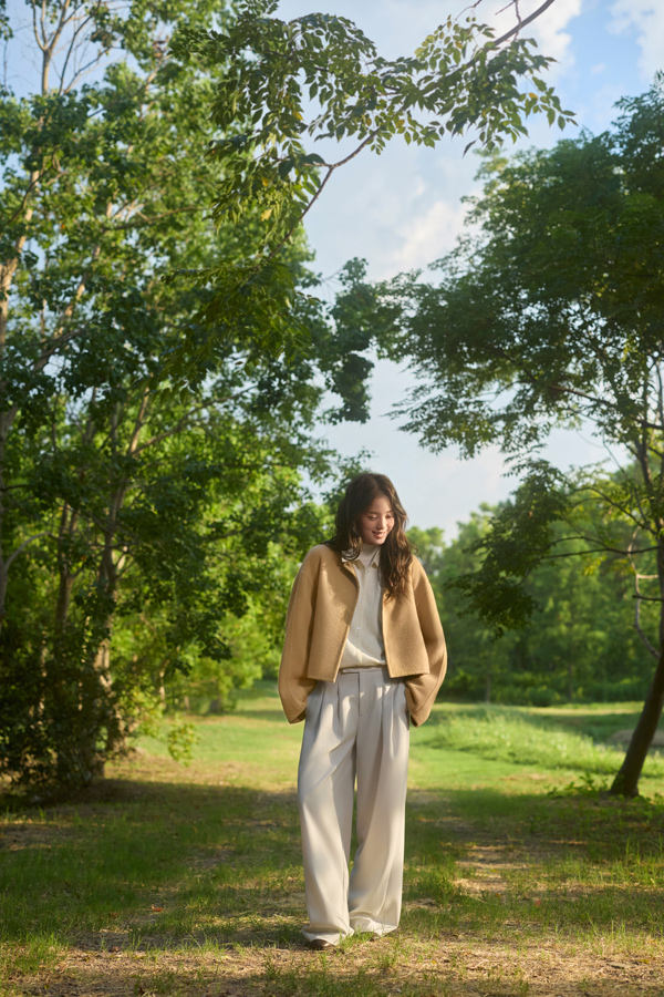 Woman in blue merino wool cardigan sitting outdoors in a natural setting.