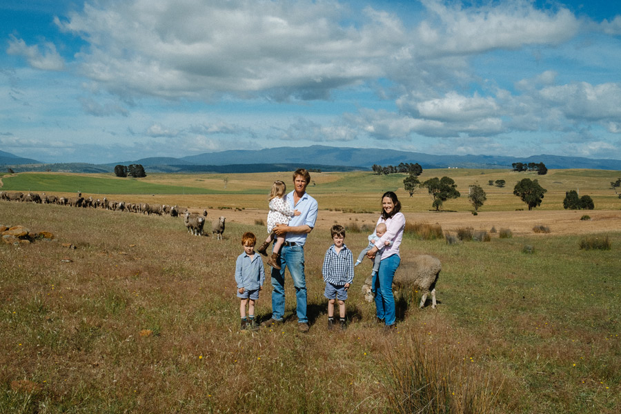 Farming family with children and sheep in an open countryside paddock under a wide blue sky