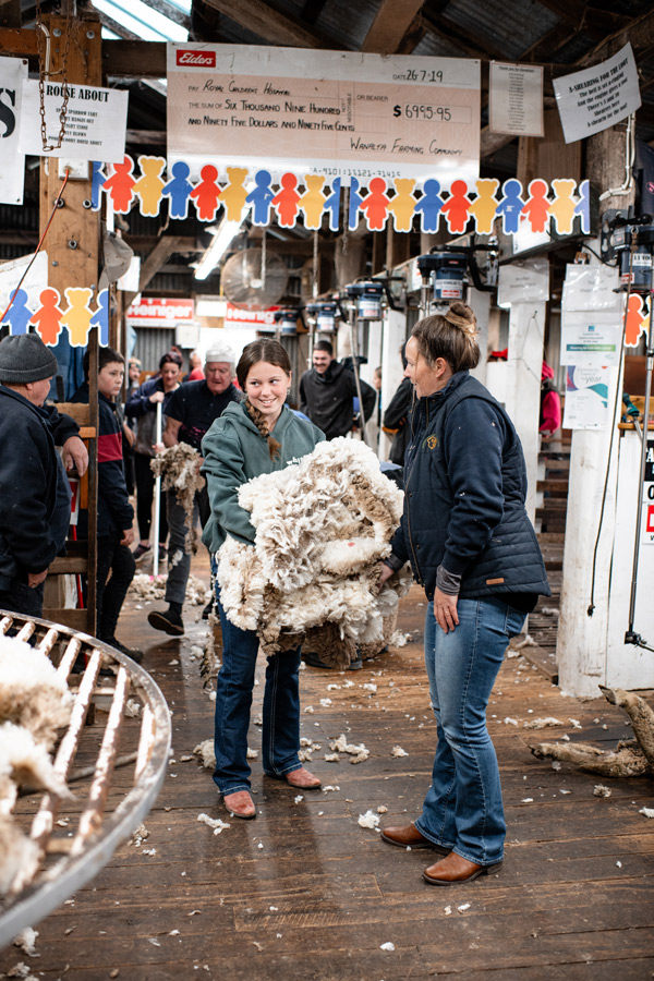 Young boy leaning out of a shearing pen giving a thumbs up inside a shearing shed