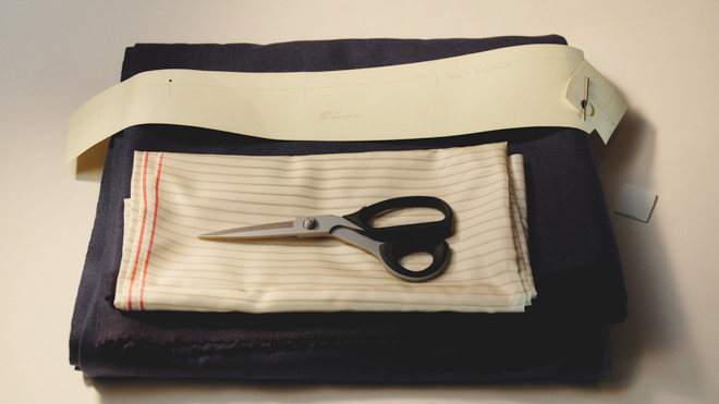 A flat lay of tailoring essentials including dark navy wool fabric, pattern paper, and a pair of professional dressmaking shears.